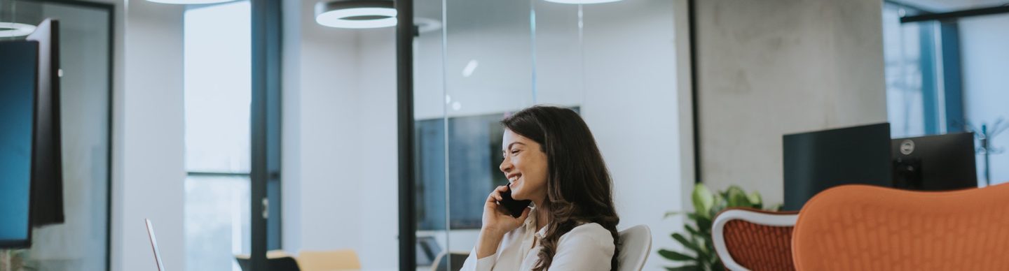 Young business woman using mobile phone while working on laptop in the modern office